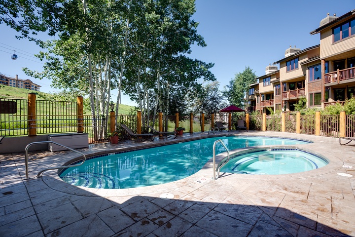 The property offers a sparkling outdoor pool and hot tub, surrounded by mature trees and rolling hillside views, perfect for unwinding after a day of mountain adventures.
