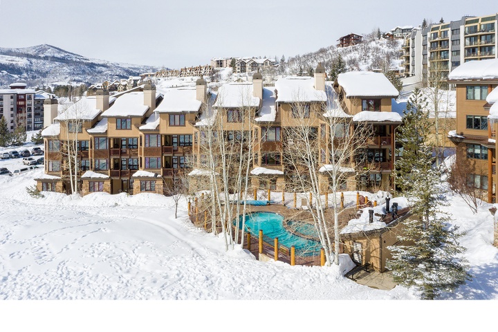 Aerial view of the property set in a scenic winter mountain resort, with ski-in access, outdoor pool, and surrounding alpine peaks blanketed in fresh snow.