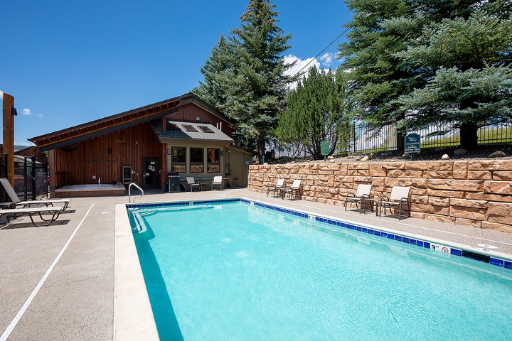 Sparkling outdoor pool framed by towering evergreens and mountain views, with cozy loungers ready for your alpine retreat.