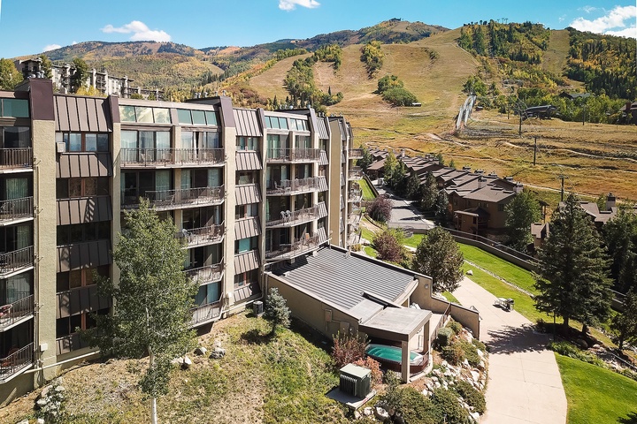Aerial view of the vacation rental property nestled in a scenic mountain valley, surrounded by rolling ski slopes, evergreen forests, and neighboring alpine lodges.