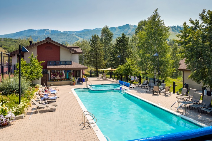 A sparkling outdoor pool framed by mountain views, with lounge chairs and shaded seating—perfect for relaxing under blue skies after a day of adventure.