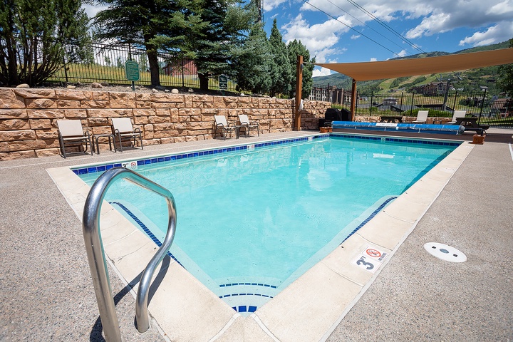 Sparkling outdoor pool framed by stone walls and mountain views, with shaded loungers ready for your sunny afternoon escape.