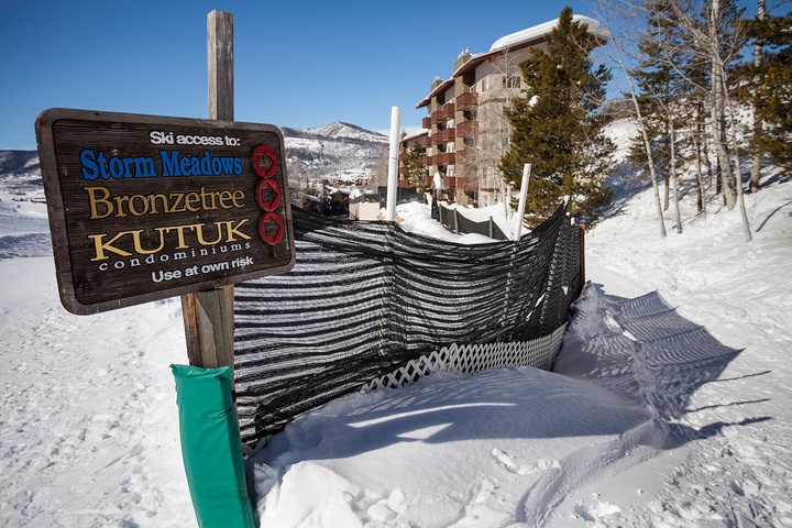 Ski access sign marks trails to Storm Meadows, Bronzetree, and Kutuk condominiums, with snowy slopes and a multi-story alpine building in the mountain setting.