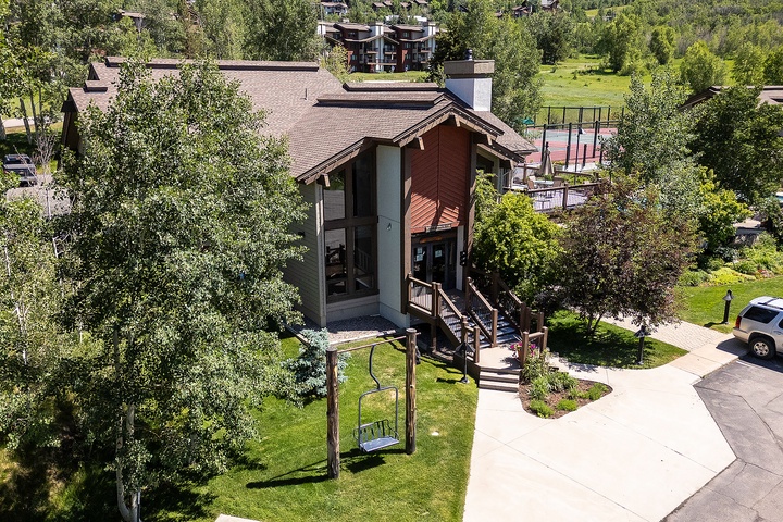 Aerial view of a charming mountain-style vacation rental surrounded by lush greenery and nearby recreational facilities including tennis courts.