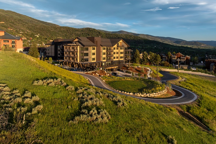 The property sits nestled among forested mountain slopes, with a winding access drive leading through landscaped grounds to the multi-story main building.