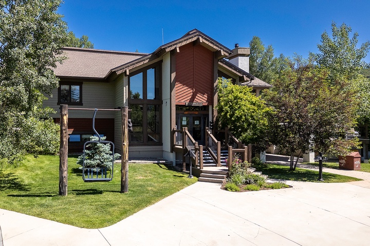 Modern mountain retreat featuring natural wood siding and expansive windows, nestled among mature trees with well-maintained landscaping and convenient driveway access.