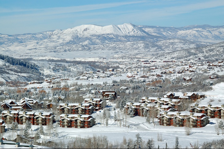 Elevated view of a mountain resort community nestled in a snow-covered valley with majestic peaks rising in the background. Seasonal winter landscape showing the property's natural alpine setting.