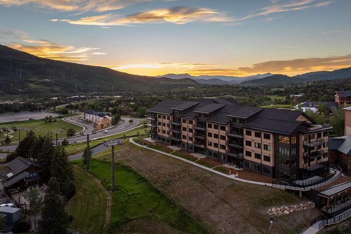 Aerial view of the property nestled in a mountain valley at sunset, showcasing the surrounding natural landscape and peaceful neighborhood setting.