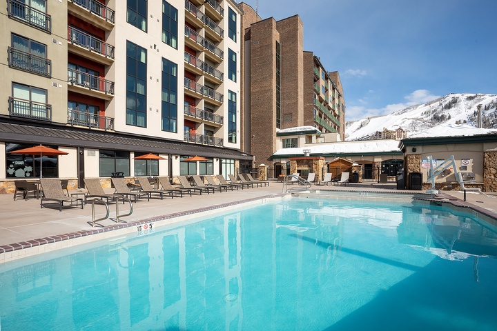 A mountain resort featuring an outdoor pool and lounge area set against snow-capped peaks, with multi-level accommodations offering ski-in/ski-out convenience.