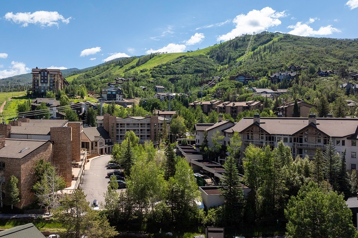 Mountain resort village nestled among evergreens with lush green ski slopes rising in the background, offering year-round outdoor recreation and scenic alpine beauty.