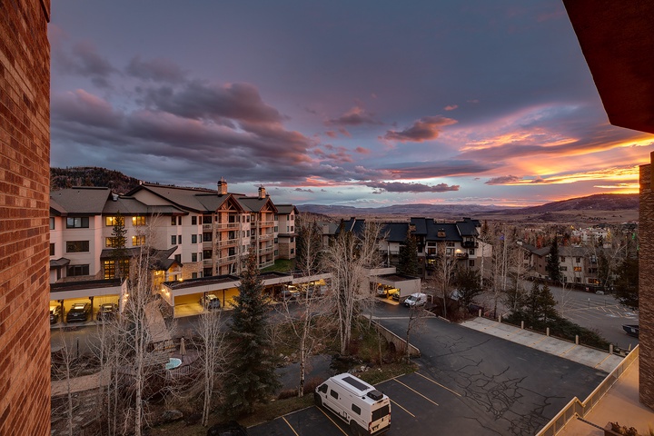 Stunning sunset over the mountain resort neighborhood, with vibrant skies painting the horizon beyond nearby lodges and parking areas.