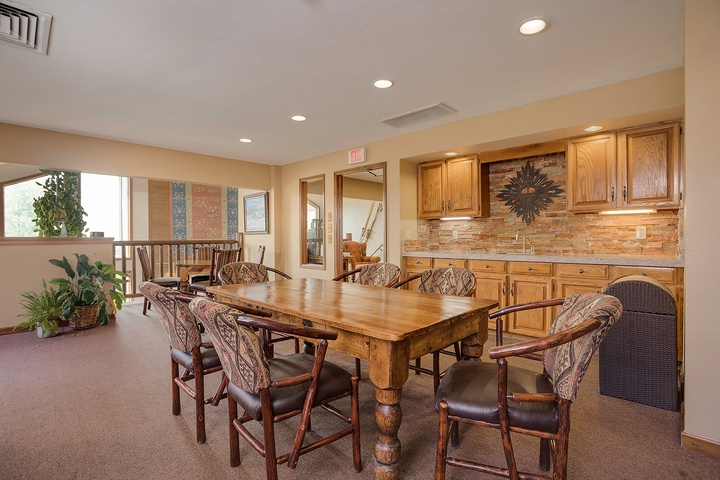Gather around this spacious dining area where your group can share meals and stories. The rustic wood table, stone backsplash, and well-equipped kitchenette create a warm communal space for unforgettable moments.