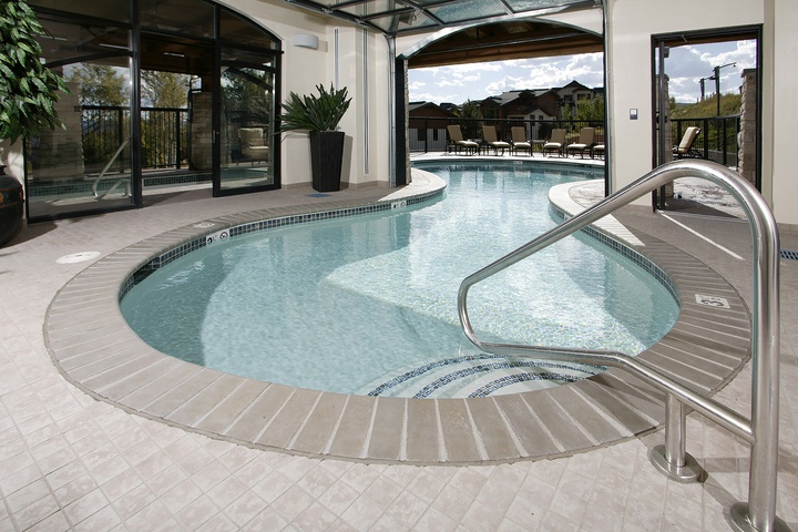 This inviting indoor-outdoor pool area flows seamlessly from the enclosed section through open archways to the sunny pool deck beyond, where lounge chairs await your relaxation under bright skies.
