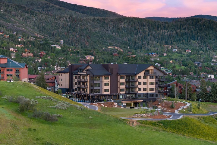 A mountain resort property nestled in a forested valley with residential buildings dotting the hillside under a soft sunset sky.