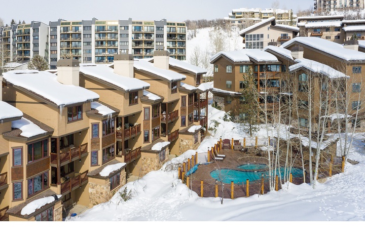A snow-dusted mountain resort community featuring alpine-style lodges, modern condominiums, and a tranquil hot tub nestled among bare aspens—your winter retreat awaits in this scenic mountain village.