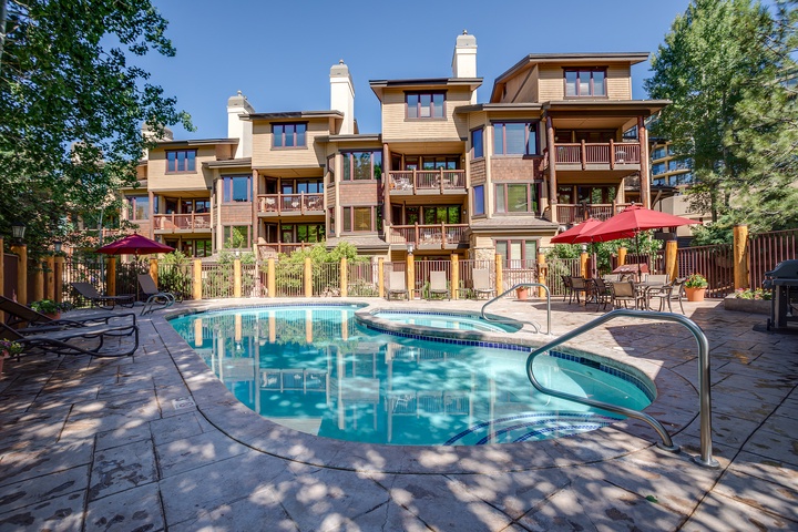 Multi-level property complex with swimming pool, patio seating, and scenic mountain backdrop—nestled in a tree-lined setting near popular area attractions.
