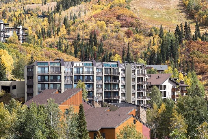 Modern multi-level buildings situated in a forested mountain valley, surrounded by evergreen and golden aspen trees during autumn season.