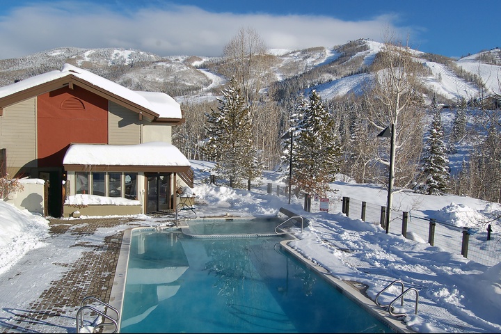 An outdoor heated pool overlooking pristine ski slopes and snowy mountain peaks, perfect for unwinding after a day on the slopes.