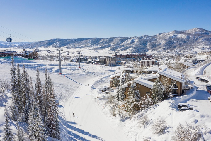 Panoramic view of a snow-covered ski resort village nestled in pristine mountain terrain, featuring slopes, gondola lifts, and accommodations set against a clear winter sky.