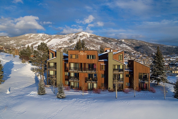 The West condominium building sits nestled in snow with ski slopes and mountain peaks creating a stunning winter backdrop in this popular resort area.