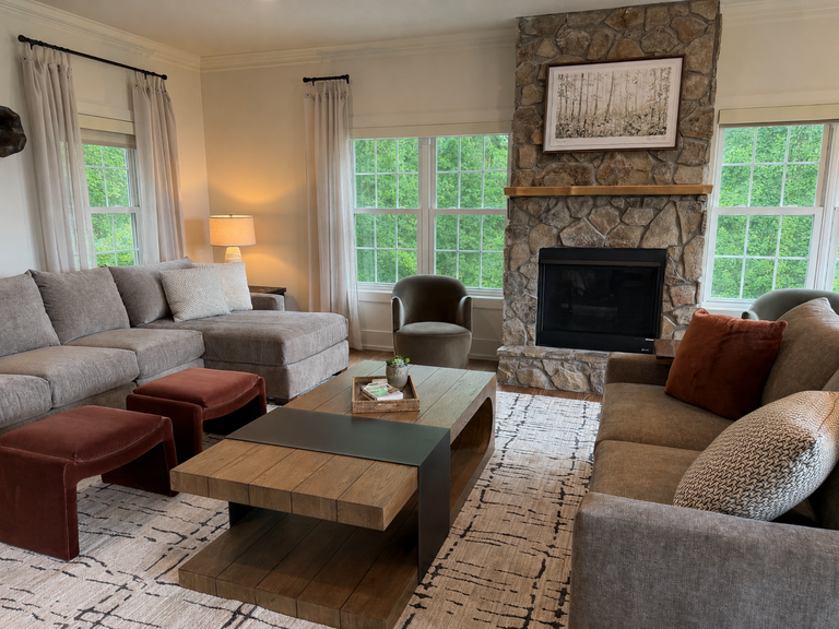 Settle into plush seating beside a cozy stone fireplace, where natural light floods through large windows revealing lush greenery. Your perfect sanctuary for unwinding after a day of adventure.