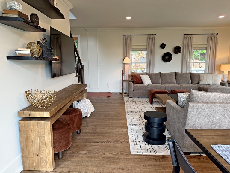 Settle into this bright, airy living room where you'll find plush sofas, warm wood accents, and natural light streaming through large windows—your perfect retreat for relaxing with loved ones.