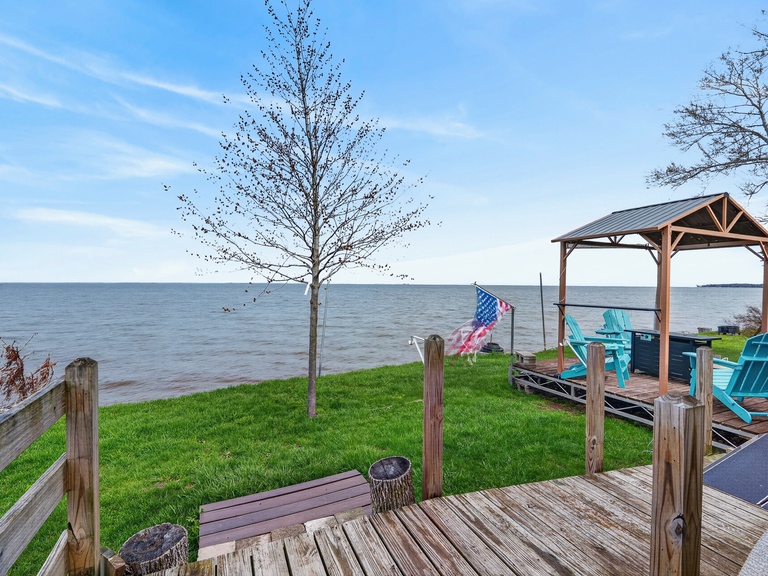 Expansive waterfront property featuring a private gazebo with turquoise seating overlooking serene lake views, complemented by lush green lawn and wooden deck areas for relaxation.