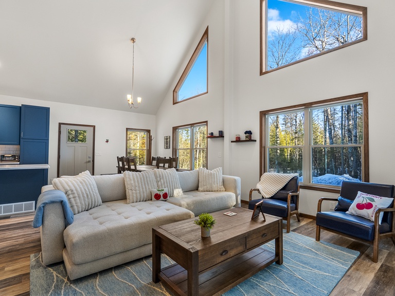 Sink into the plush sectional as natural light floods through soaring windows, revealing peaceful forest views from your bright, airy living space.