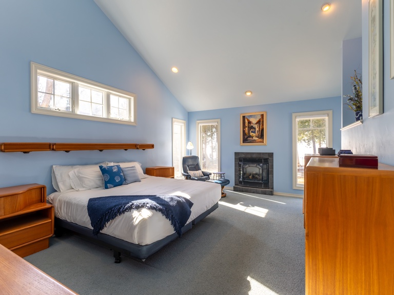 Just off the living room - Unwind in your serene Primary suite with warm wooden furnishings, soaring ceilings, and gas fireplace, perfect for peaceful relaxation.