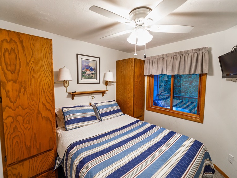Primary bedroom includes a queen bed, ceiling fan, TV, room darkening shades, hangers and extra blankets