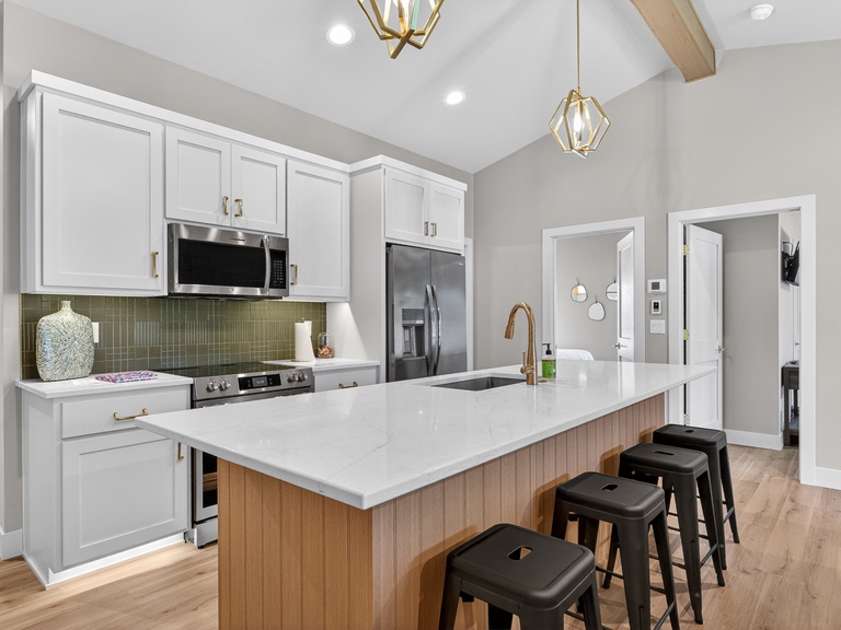 Upper Unit Kitchen-This bright, modern kitchen features sleek white cabinetry, gleaming quartz countertops, and stainless steel appliances. Gather around the spacious island with stylish seating—perfect for your morning coffee or evening meals together.