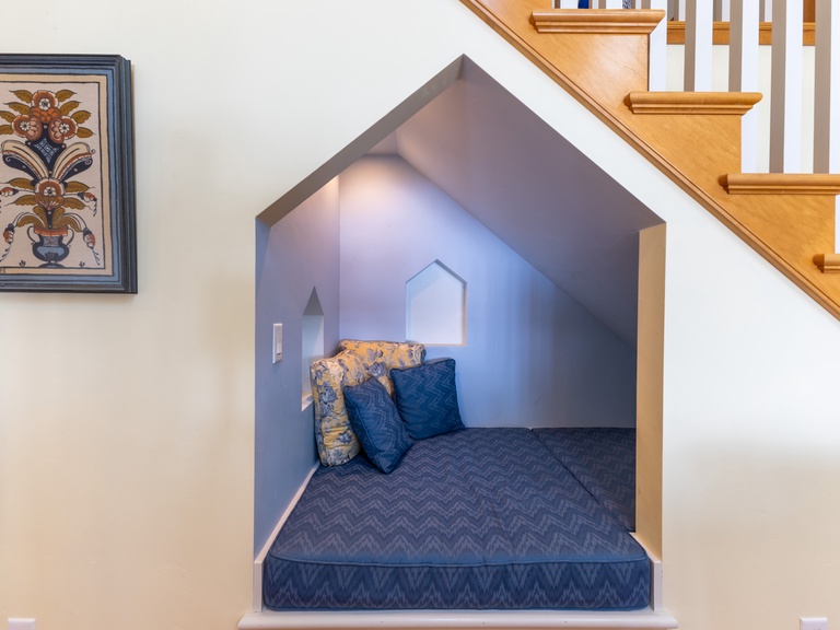 Your magical hideaway awaits beneath the stairs, where cozy blue bedding and soft pillows create the perfect reading nook.