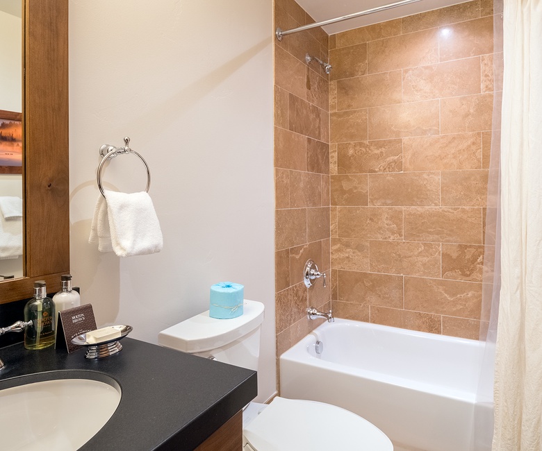 A pristine bathroom features warm travertine tile, a deep soaking tub, and a polished vanity with thoughtful touches—your private spa awaits.