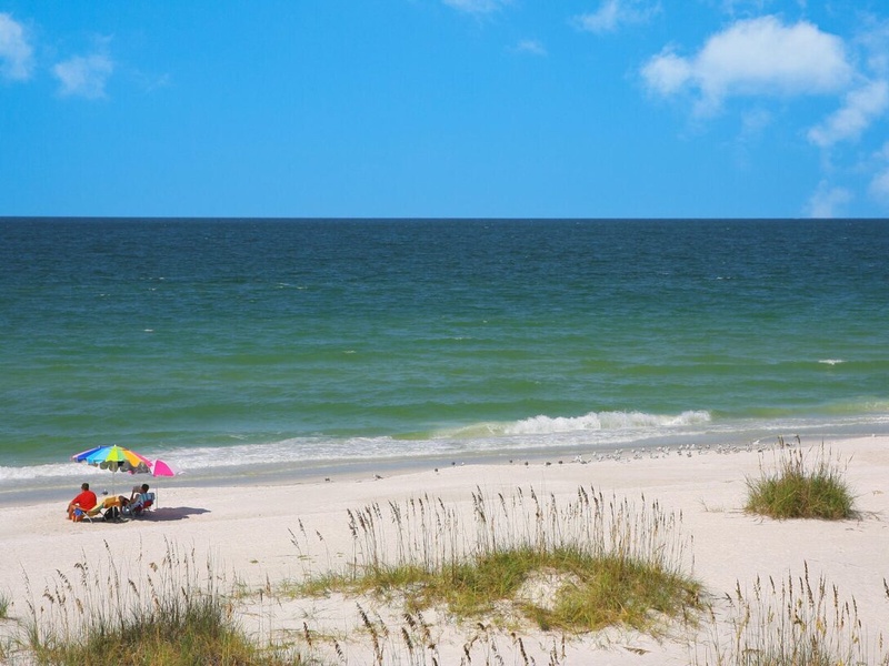 Pristine sandy beach stretches along turquoise waters under a brilliant blue sky with fluffy white clouds.