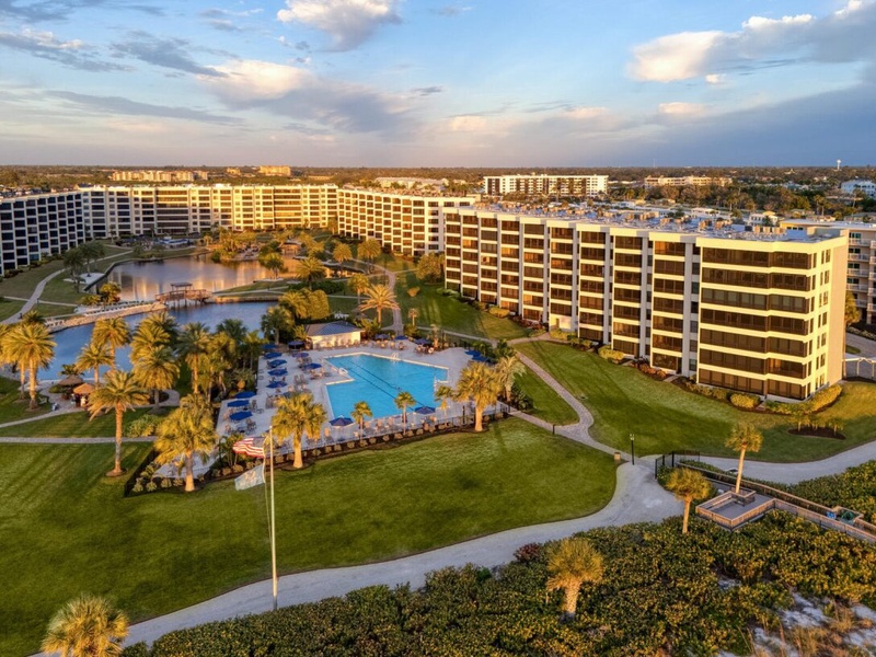 Expansive resort complex with curved high-rise buildings surrounding a pristine swimming pool and lake, set amid tropical landscaping.