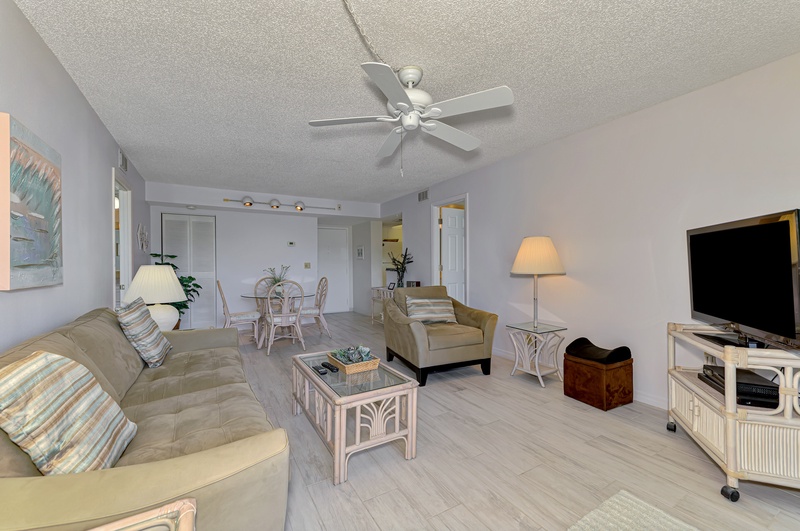 Relax in your spacious living area with coastal-style furnishings, ceiling fan, and modern entertainment setup for perfect downtime.