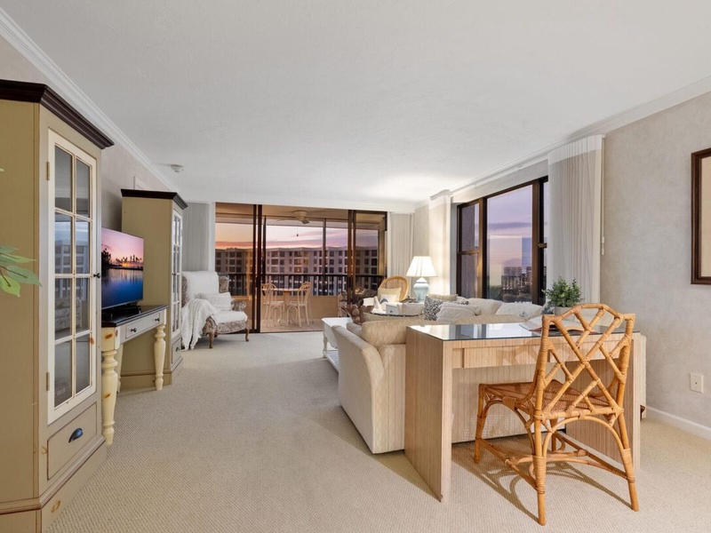 Relax in your spacious living area with elegant furnishings and floor-to-ceiling windows showcasing stunning city views at sunset.