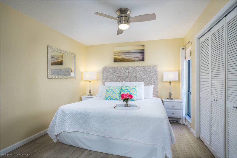 Drift off under warm yellow walls and gentle ceiling fan breezes in your serene bedroom sanctuary with ocean artwork creating peaceful vibes.