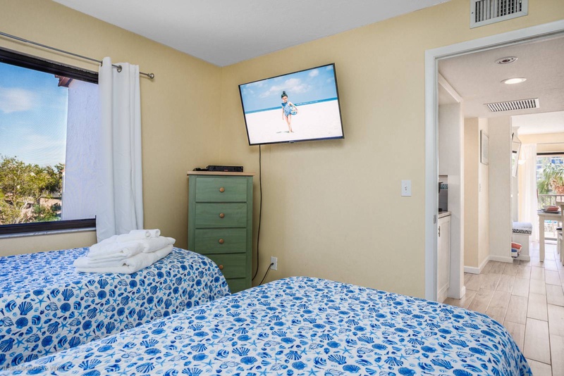 Your peaceful bedroom features twin beds with ocean-inspired linens, wall-mounted TV, and storage for your vacation essentials.