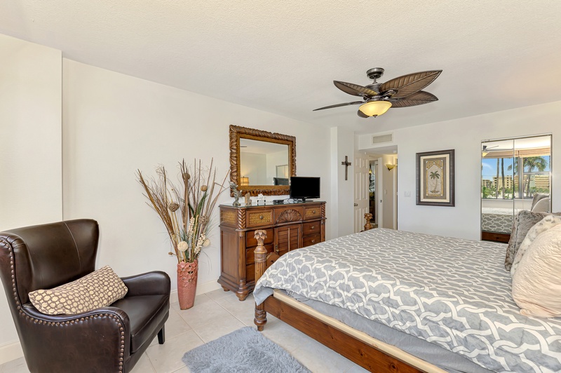 Relax in your elegant bedroom with tropical ceiling fan, comfortable seating area, and palm tree views from your private balcony.
