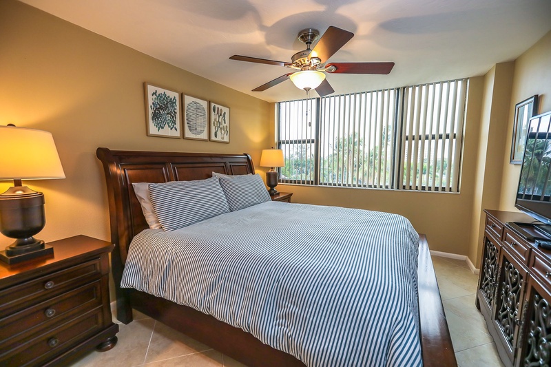 Rest peacefully in your cozy bedroom with elegant dark wood furnishings, crisp striped linens, and gentle ceiling fan breeze keeping you comfortable.