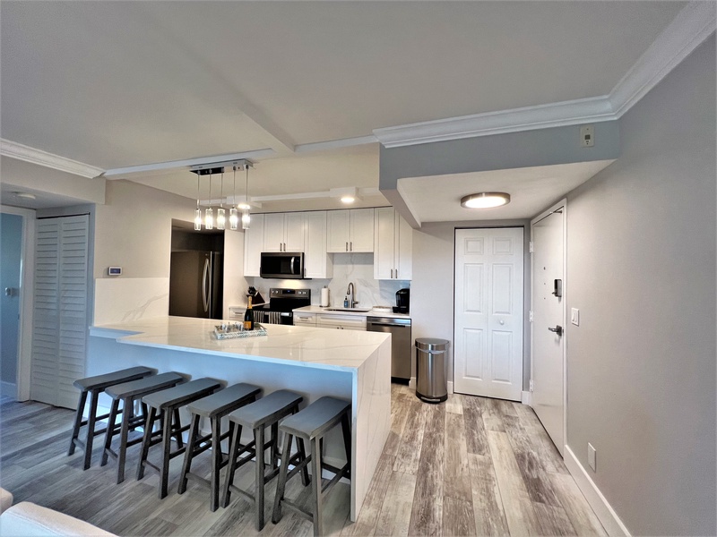 Your modern kitchen awaits with sleek white cabinets, gleaming countertops, and a spacious breakfast bar perfect for morning coffee or evening meals.