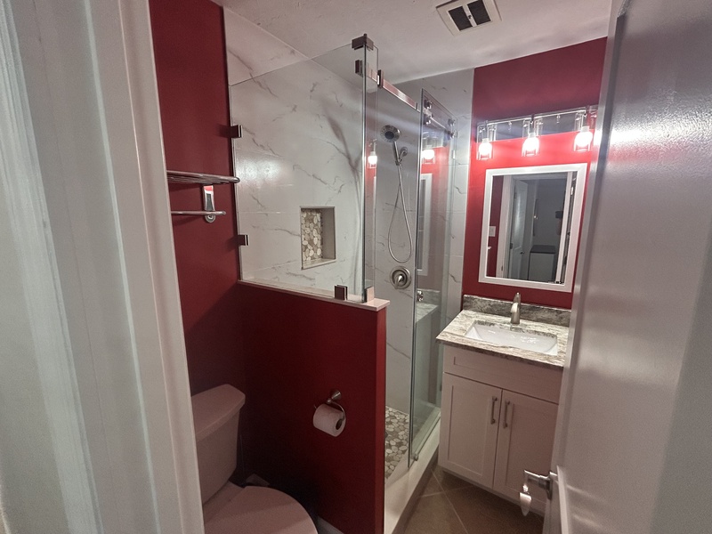 Refresh in your modern bathroom featuring a spacious glass shower, elegant marble accents, and stylish red design touches.