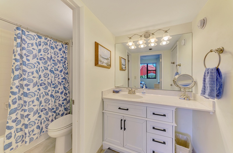 Your private bathroom features coastal charm with seashell shower curtain, crisp white vanity, and Hollywood-style lighting for perfect morning routines.