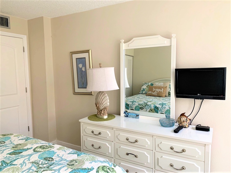 Relax in your coastal-themed bedroom with twin beds, elegant white furniture, and convenient TV entertainment for peaceful nights.