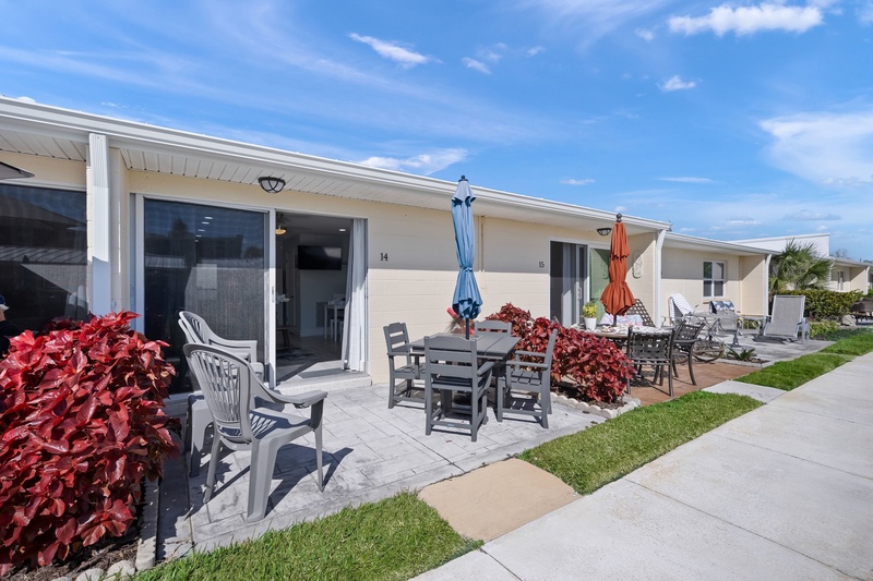 Stylish modern property featuring individual units with private patios, outdoor dining areas, and vibrant landscaping under sunny skies.