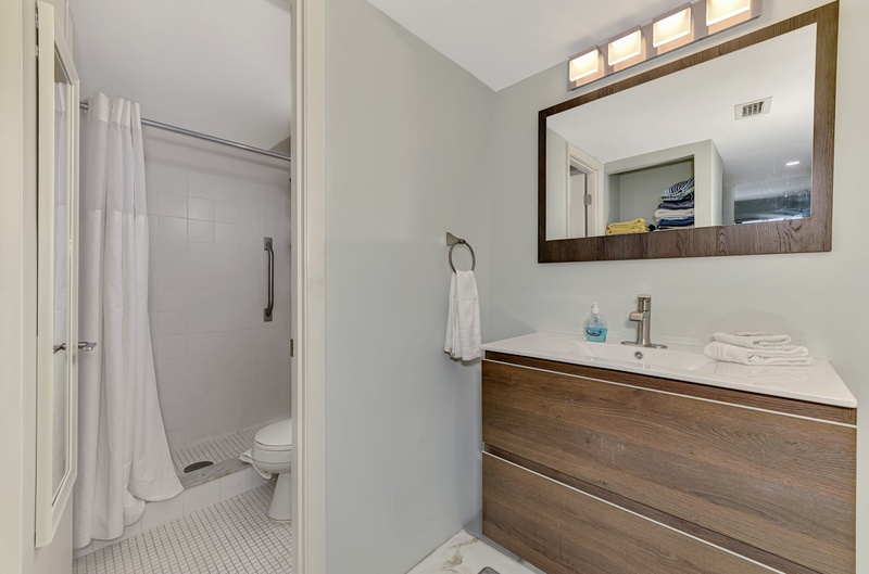 Step into your pristine bathroom featuring modern wood vanity, spacious shower, and fresh towels waiting for your arrival.