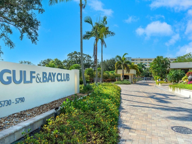 Gulf & Bay Club's welcoming entrance features tropical landscaping with towering palms and lush gardens leading to the property.