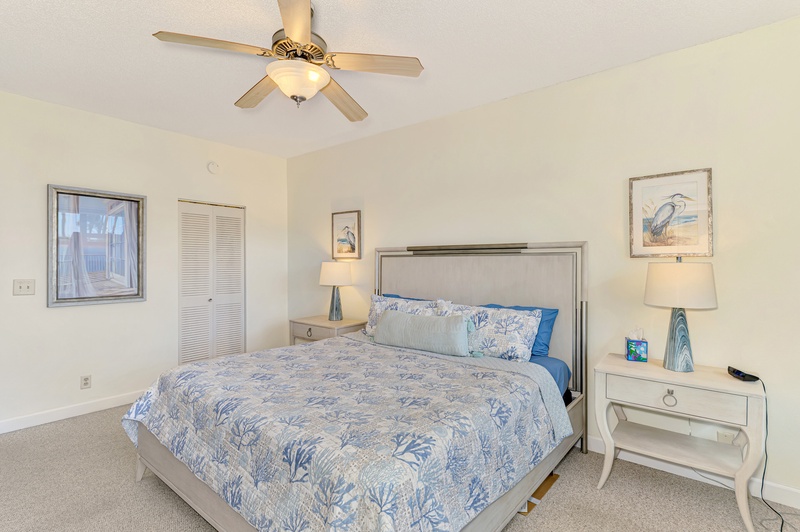 Drift off in your peaceful bedroom with coastal blue bedding, gentle ceiling fan, and nautical artwork creating the perfect seaside retreat.