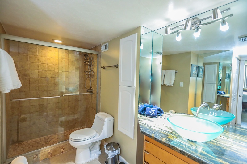 Your private bathroom features a spacious walk-in shower, modern glass vessel sink, and elegant stone countertops for your comfort.